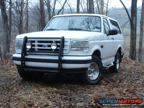White 1995 Ford Bronco with bull bar parked on a dirt road in woods