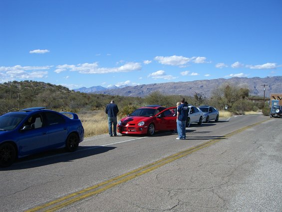 Red Dodge Neon SRT-4 with door open, parked on roadside with a blue Dodge Neon SRT-4 and other cars behind it