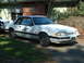 1987 Ford Mustang - A white 1987 Ford Mustang police car is parked in a driveway, displaying a "5.0" badge on its fender.