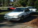 1987 Ford Mustang - A white 1987 Ford Mustang coupe is parked in front of another vehicle, displaying a distinctive decal on its door.