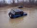 1974 Ford Bronco - A blue 1974 Ford Bronco is partially submerged in muddy water, with another SUV parked nearby.