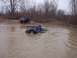 1974 Ford Bronco - A blue Jeep Wrangler is stuck in a muddy puddle while another SUV waits on the bank.
