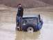 1974 Ford Bronco - A man stands on the side of a blue off-road vehicle stuck deep in muddy water, holding tow straps.