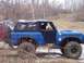 1974 Ford Bronco - A blue 1974 Ford Bronco navigates a muddy off-road course with another vehicle in the background.
