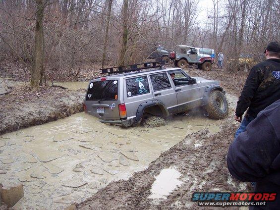 Silver Jeep Cherokee XJ stuck in a muddy ditch with other Jeeps nearby