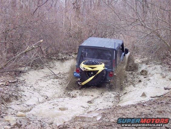 Black Jeep Wrangler with yellow tow strap on spare tire driving through mud