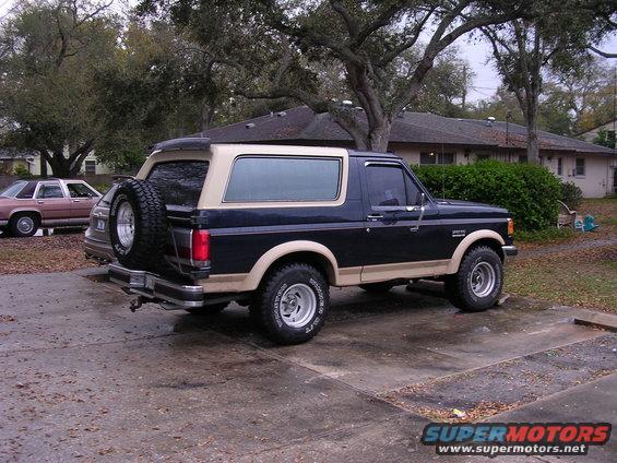 Dark blue and tan Ford Bronco with a spare tire on the back, parked on a wet driveway