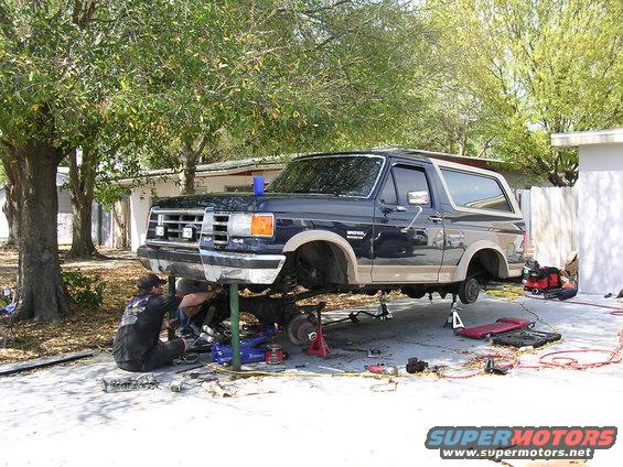 Dark blue 1988 Ford Bronco on lift with mechanics working underneath