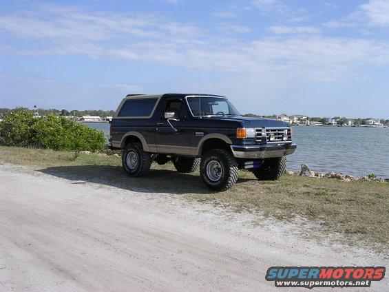 dark blue Ford Bronco parked by the water, lifted with large tires