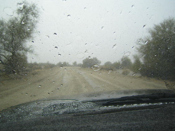 Interior view of a dusty road through a rain-streaked windshield