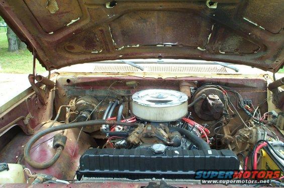 Engine bay of a rusty red truck with an open hood, showing the V8 engine, air filter, radiator, and wiring