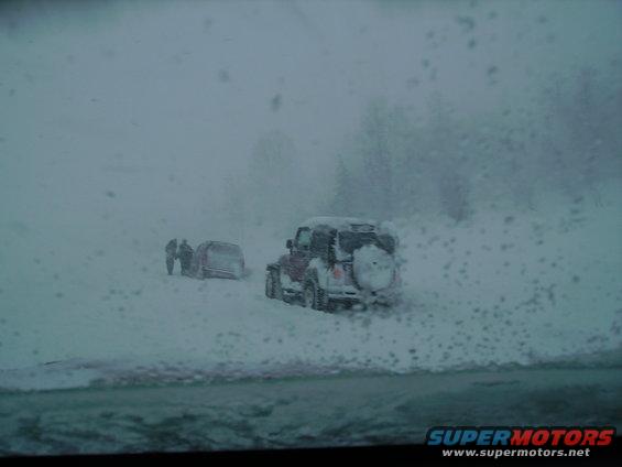 Two SUVs stuck in deep snow with people standing nearby