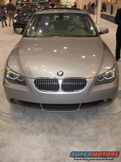 Front view of a silver BMW sedan at a car show. Another dark car is visible behind it