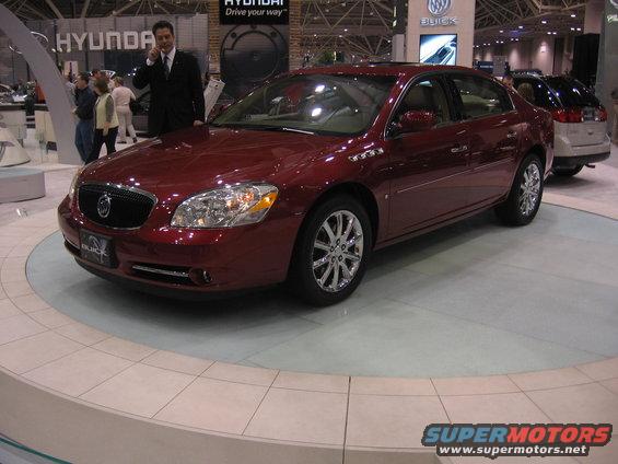 Red Buick sedan on display, with a man in a suit talking on phone behind it. Another SUV is parked behind