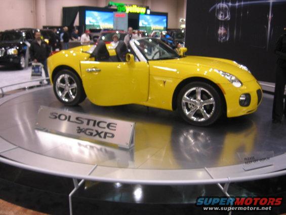Yellow Pontiac Solstice GXP convertible on display stand at an auto show