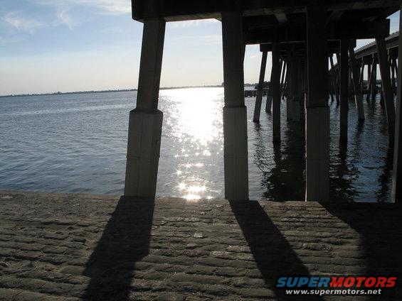 Concrete pier pilings rise from the water under a bright sun