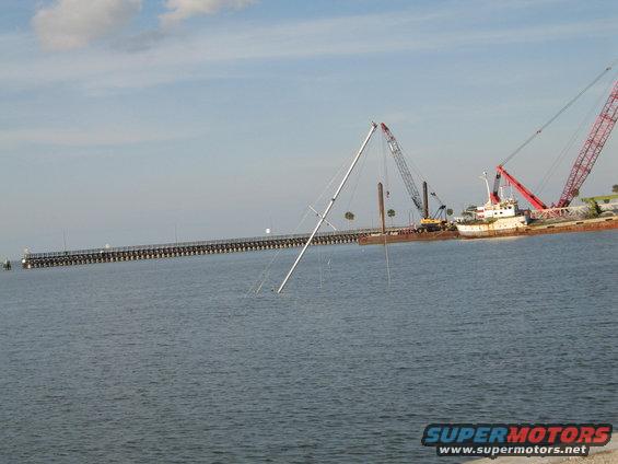 Sunken sailboat mast in water with construction barges and cranes in background