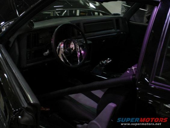 car interior showing steering wheel, dashboard, roll cage, and racing seats