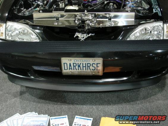 Front view of a black car with an open hood, running horse emblem, and DARKRHSE license plate