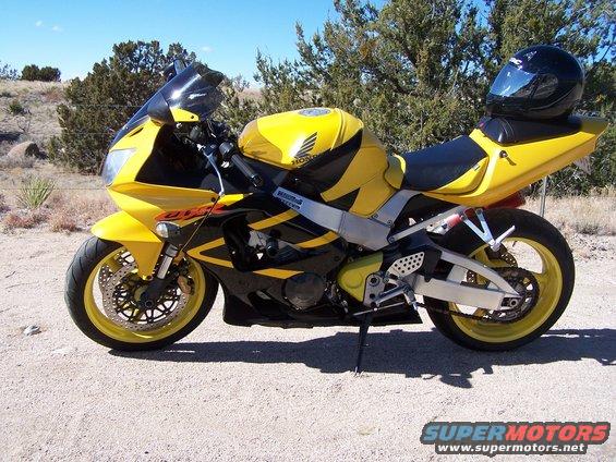 Yellow and black 2000 Honda CBR-RR motorcycle parked on a dirt road, with a black helmet on the seat