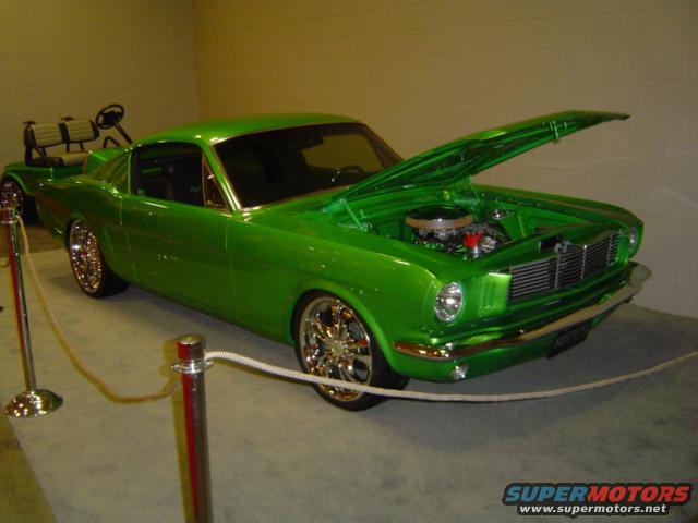 Green custom car with hood open, showing engine. A golf cart is behind it