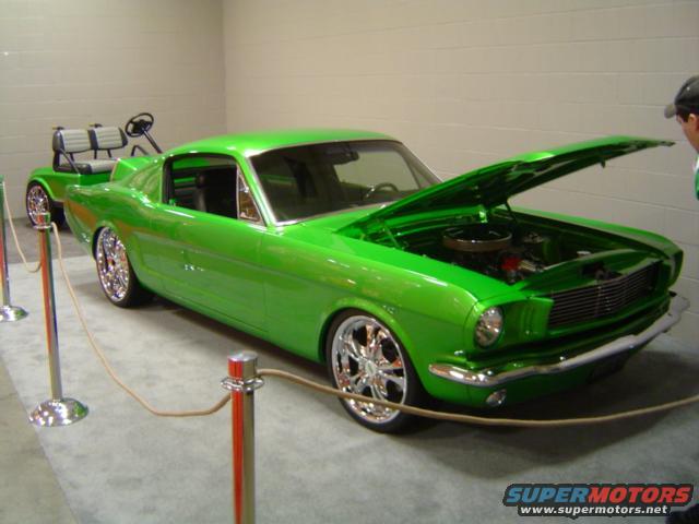 Green 1965 Ford Mustang with hood open, chrome wheels, and a golf cart behind it