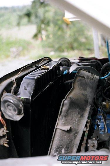 Radiator and engine components under an open hood. A black plastic shroud is visible
