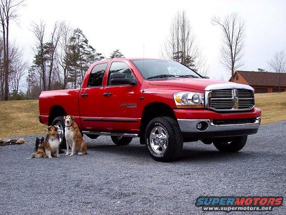 Red 2006 Dodge 2500 pickup truck parked outside with three dogs sitting in front