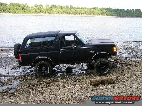 Black Ford Bronco parked on a rocky shore by a river
