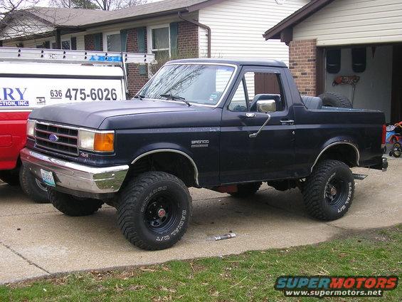 Dark blue 1990 Ford Bronco, lifted, with off-road tires, parked in driveway