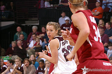 women in basketball uniforms on court, crowd in background