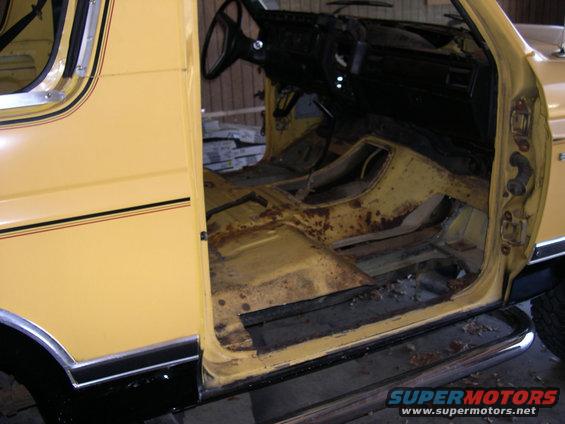 Yellow SUV interior with rusted floorboards and exposed metal, viewed from the side