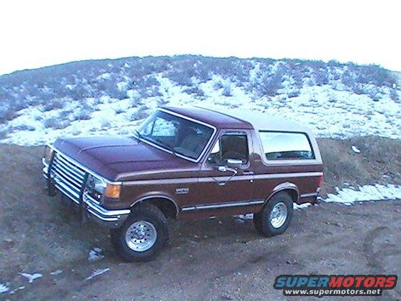 Maroon Ford Bronco parked on dirt with snowy hills in background