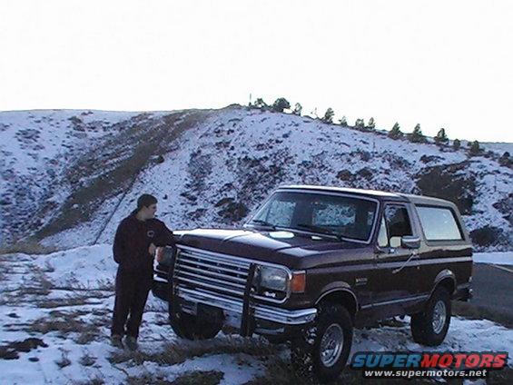 Guy leaning on a maroon Ford Bronco in a snowy landscape