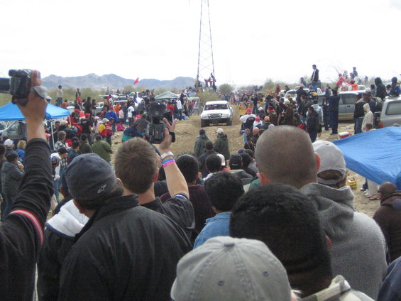White SUV on dirt road, crowd watching