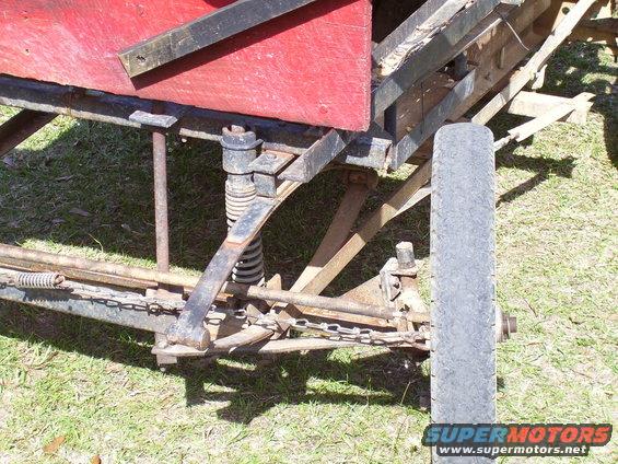Vehicle chassis with leaf springs, coil spring, and tire. Red body panel visible