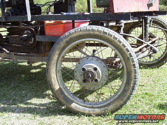 Close-up of a spoked wheel and tire on a custom-built vehicle, with another wheel visible in the background