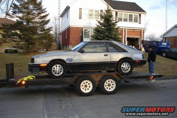 Silver and black 1981 Ford Mustang RS Turbo on trailer, man standing behind it