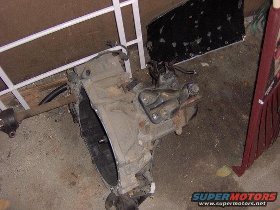 Car transmission assembly with attached driveshaft, resting on a concrete floor