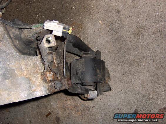 Close-up of a rusty engine mount bracket with a wiring connector attached