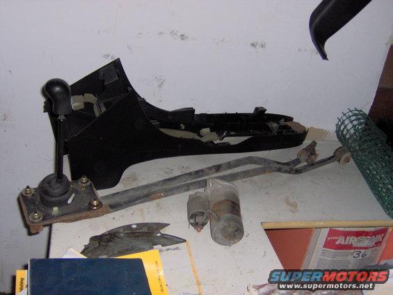 Car parts laid out on a table: shifter assembly, linkage, starter motor, and dashboard trim piece