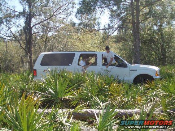 White 2000 Ford Excursion parked in dense foliage, with two people visible in the windows