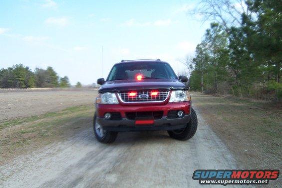 Red Ford Explorer with red and white emergency lights on the roof and grille, parked on a dirt road