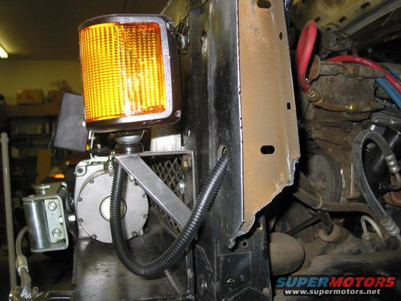 Close-up of a vehicle's front end with an amber warning light and some engine components visible