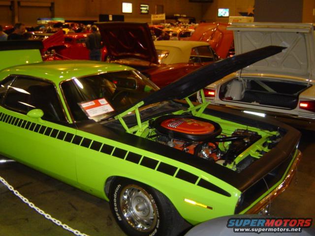 Lime green muscle car with black stripes and hood open, showing engine. Other cars in background