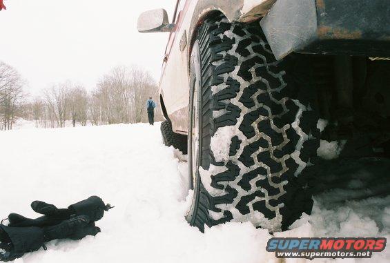 Red and white Ford Bronco in snow, close-up on aggressive tire tread, side view