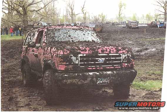 Mud-covered red SUV, front view, with a grille resembling a 1992 Ford Bronco
