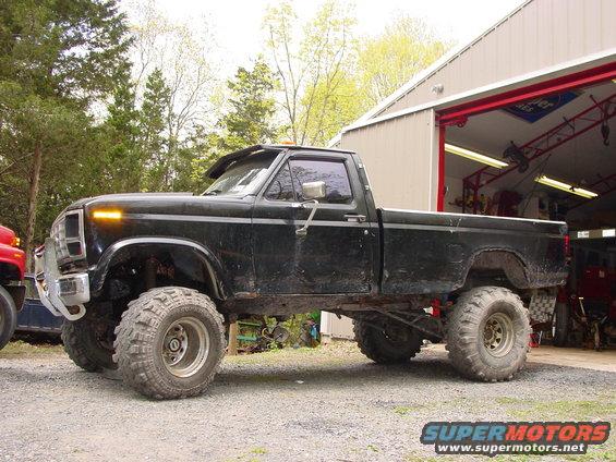 Lifted black pickup truck with large off-road tires parked in front of a garage