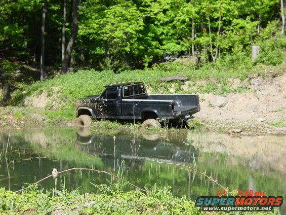 Black pickup truck stuck in water, side view. Appears to be from the 1980s