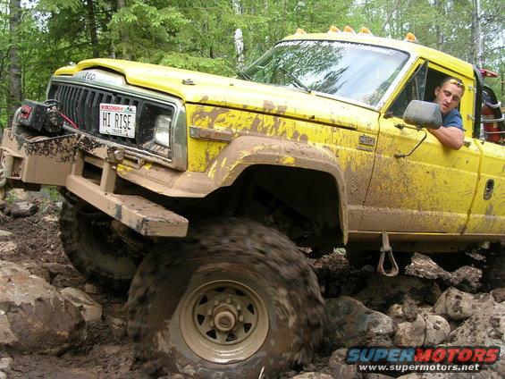 Yellow 1986 Jeep J-10 off-roading on rocks and mud